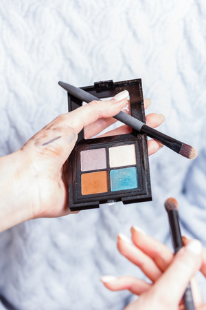 A palette of eye shadows and makeup brushes in the hands of a make-up artist with traces of cosmetics testsの写真素材