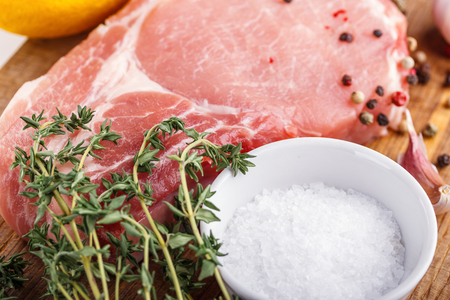 Raw pork natural cutlet with beam thyme, garlic, salt, pepper, salt and pepper shakers on the wooden cutting board closeupの写真素材