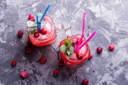 Berry Morse, cocktail of currant and cowberry with ice and fresh mint leaves, with powdered sugar in cocktail drinking jars with colored drinking straws on a concrete table top viewの写真素材