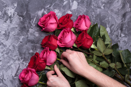Florist collects a bouquet of red roses on a gray concrete table close-up