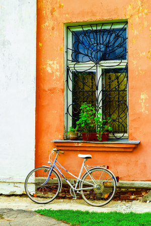 Old bicycle on a wall background with old, cracked plaster and a window with flowers.の写真素材