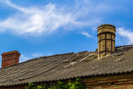 The roof, covered with old slate, with old and new chimneys made of bricks against the background of the blue cloudy skyの写真素材