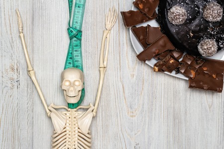 Chocolate cake and slices on a plate and skeleton on a wooden table. Flat lay. Obesity Death Conceptの写真素材