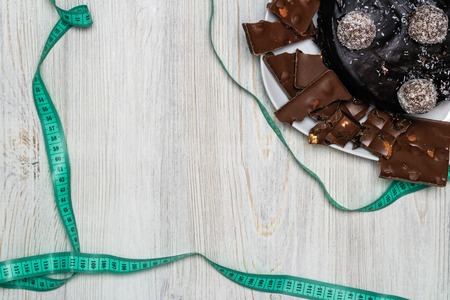 Chocolate cake, slices of chocolate on a plate and a measuring tape top view. The concept of choosing between harmful food and a healthy lifestyle. Flat lay. Copy space.の写真素材