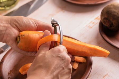 Cook cleans carrots with a peeler close-up. Organic cooking concept.の写真素材