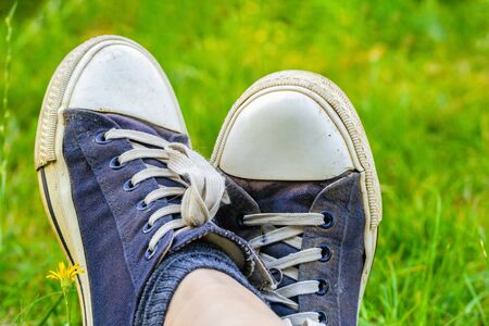 Legs in old, dirty, shabby sneakers on the green grass. Tourist and travel concept.の写真素材