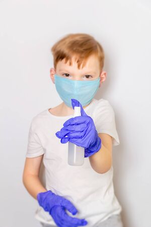 Seven year old boy in a medical mask and latex gloves with an antiseptic spray on a white background. Caronavirus Protection Concept.の写真素材