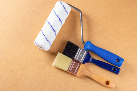 Brushes with wooden handles and a paint roller on a fiberboard. Copy space. Top view. High quality...