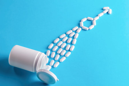 Male health medical concept. Pills are poured out of a bottle and stacked in a male gender symbol on a blue backgroundの写真素材