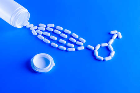 Erectile dysfunction therapy medical concept. Pills are poured out of a bottle and stacked in a male gender symbol on a blue backgroundの写真素材