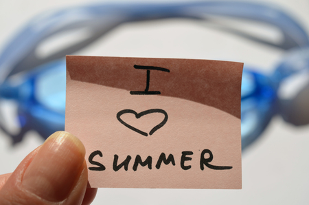 hand of a woman with fingers holds blue goggles for pool with pink sticker with text lettering inscription I love summer, tonedの写真素材
