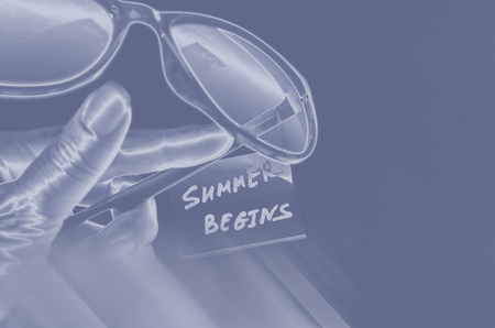hand of a woman with fingers holds sunglasses lying on background with silver sticker with text lettering inscription summer begins, tonedの写真素材