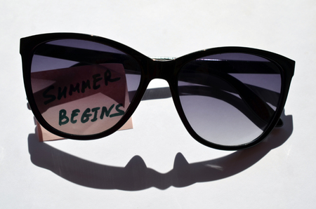 sunglasses lying on background with pink sticker with text lettering inscription summer begins, tonedの写真素材