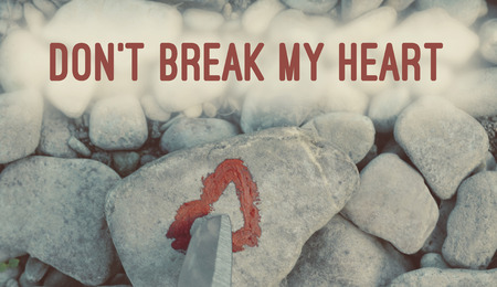 Cutting knife diving pink heart painted with lipstick on piece of stone. Symbol of the end of love and of two people break up and divorce with text letter Don't break my heartの写真素材