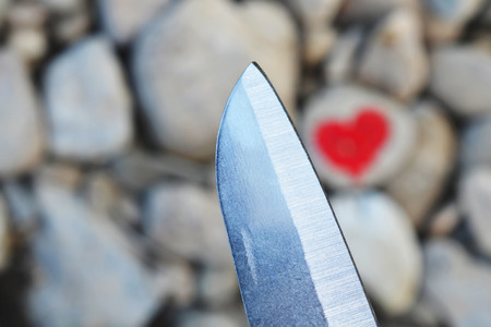 Cutting knife diving pink heart painted with lipstick on piece of stone. Symbol of the end of love and of two people break up and divorceの写真素材