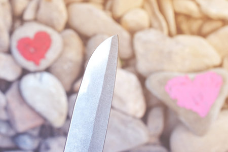 Cutting knife diving pink heart painted with lipstick on piece of stone. Symbol of the end of love and of two people break up and divorceの写真素材
