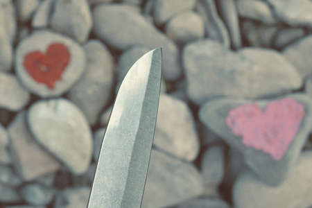 Cutting knife diving pink heart painted with lipstick on piece of stone. Symbol of the end of love and of two people break up and divorceの写真素材
