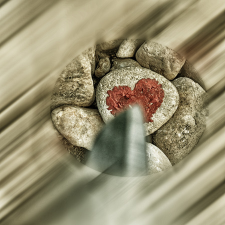 Cutting knife diving pink heart painted with lipstick on piece of stone. Symbol of the end of love and of two people break up and divorceの写真素材