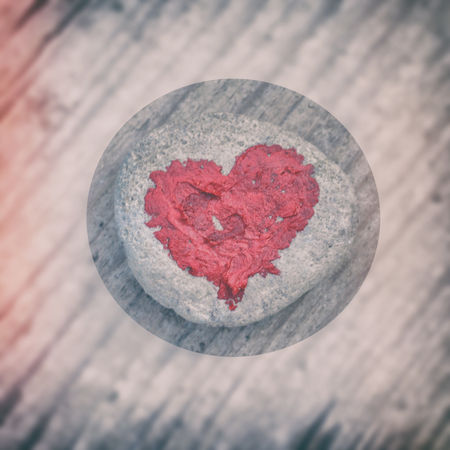 Pink heart painted with lipstick on piece of stone on background of wooden boardの写真素材