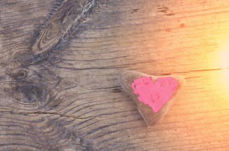 Pink heart painted with lipstick on piece of stone on background of wooden boardの写真素材