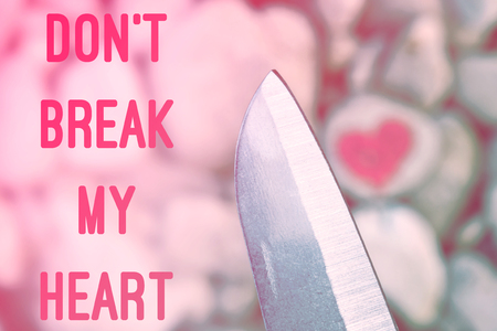 Cutting knife diving pink heart painted with lipstick on piece of stone. Symbol of the end of love and of two people break up and divorce with text letter Don't break my heartの写真素材