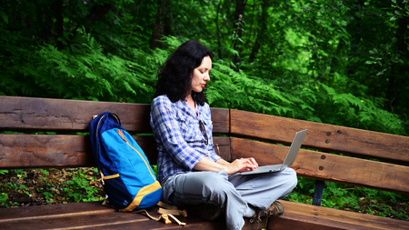 Traveling woman using laptop in park. Concept of freelance work in travelling working on natureの写真素材