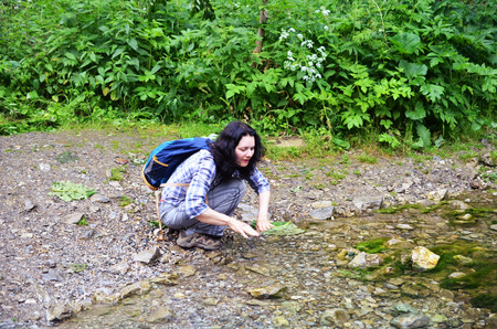 Traveling woman washing her face and hands with water from stream in forest. Girl sits with backpackの写真素材
