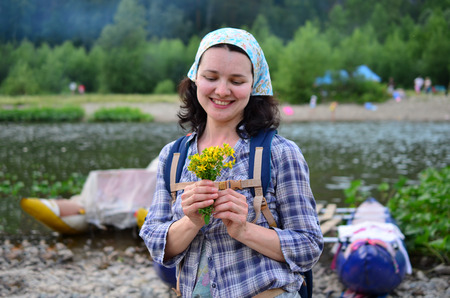Traveling girl smells yellow flowers taken from nature on background of riverの写真素材