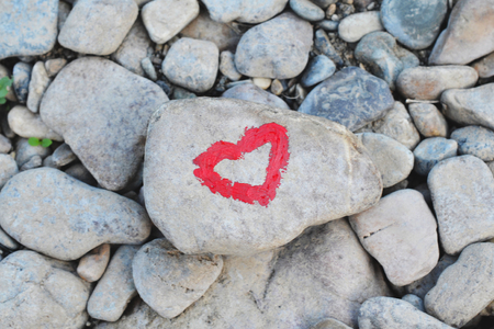 Pink heart painted with lipstick on piece of stone on background of many small stonesの写真素材