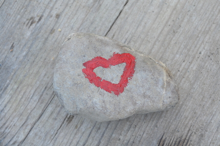 Pink heart painted with lipstick on piece of stone on background of wooden boardの写真素材