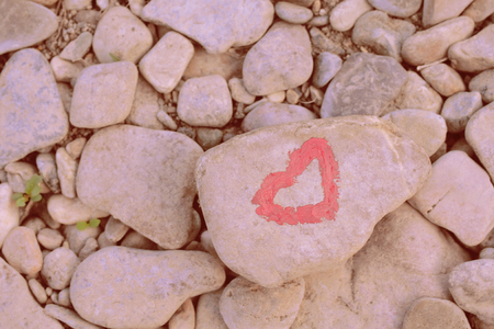 Pink heart painted with lipstick on piece of stone on background of many small stonesの写真素材