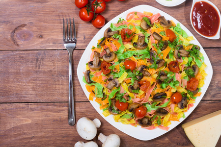 Colored pasta with mushrooms , tomatoes and cheese . On wooden backgroundの写真素材