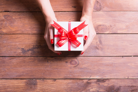 Woman holding a christmas gift in hand on wooden background