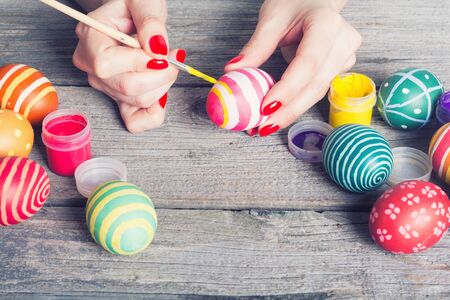 Woman painting easter eggs on wooden background