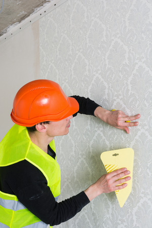 Handyman with spatula putting up wallpaper on the wallの写真素材