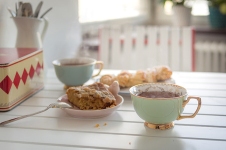 Two cups of hot tea with two cakes on white table in the morning light.の写真素材