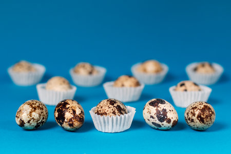 Variegated quail eggs lie on the table and in white paper rosettes. Blue background. Easter. Close-up.の写真素材