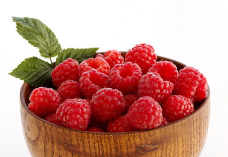 Bright, juicy berries of a garden raspberry with a green leaf in a wooden cup on a white background. Isolated. Close-up.の写真素材