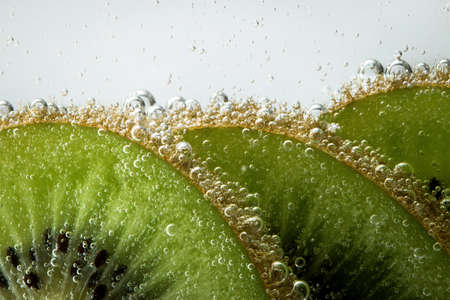 Slices of green, ripe kiwi in the water with bubbles behind the glassの写真素材