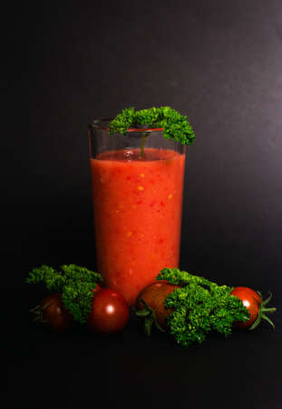 Tomato juice in a glass cup, cherry tomatoes and green leaves of parsley on a black background. close-up. Isolated, Vegetarianism.の写真素材