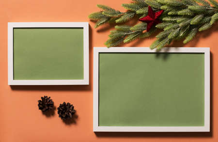 Two white frames with a green background for the inscription on the red surface. Spruce branches are decorated with a red star. Christmas background.の写真素材