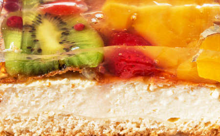 Fruit cheesecake slice texture. Green kiwi, yellow mango, red berries are covered with transparent jelly on a bun. Close-up.の写真素材