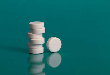 A column of pharmaceutical white pills on a bright green background. Creative concept of medicine. Minimalist style with colorful paper background. Trendy colors. Isolated.の写真素材