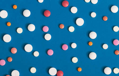 Many multi-colored pills on a blue background as a prescription treatment concept. Varieties of painkillers and antibiotics, allergies to drugs. Close-up.の写真素材
