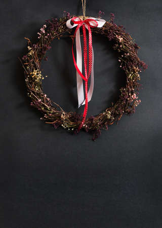 Easter home decoration. Wreath of birch branches with white and red silk ribbons and flowers. Gray wall background, empty space for an inscription. Spring decoration.の写真素材