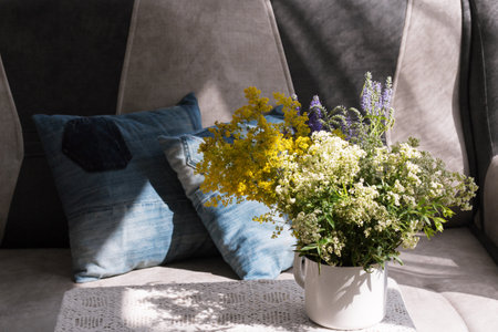 Interior. Room. Bouquet of white, field flowers in iron, rough. a white mug on a table covered with a lace tablecloth. Sofa, pillows from old jeans. Summer. Cosiness. Rustic. Country house.の写真素材