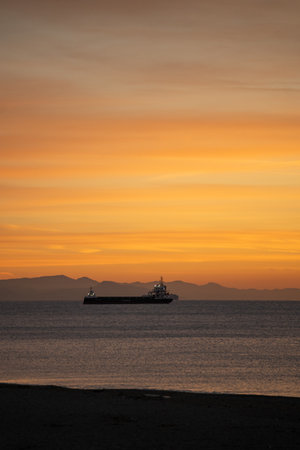 vast maritime morning, serene dawn over oceanic expanse, gentle sunrise casting glow on peaceful waters, calm seascape at dawn with distant mountainous backdropの写真素材