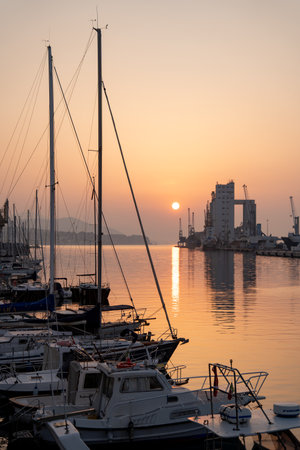 Yachts and tall cranes mirrored in tranquil sunrise watersの写真素材