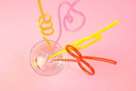 Multicolored plastic cocktail straws in glass on a pink background. Concept: holiday, party, ecology, plasticの写真素材