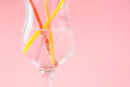 Multicolored plastic cocktail straws in glass on a pink background. Concept: holiday, party, ecology, plasticの写真素材